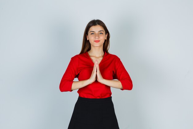 Junge Dame in der roten Bluse, Rock, der namaste Geste zeigt und friedlich aussieht