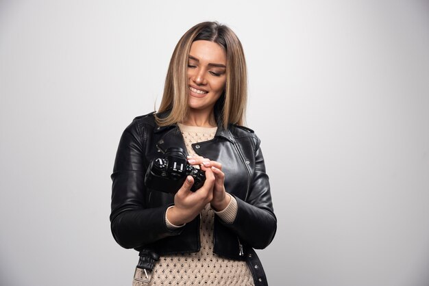 Junge Dame in der schwarzen Lederjacke, die Fotos mit Kamera auf positive und lächelnde Weise macht