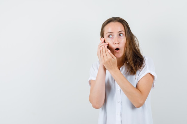 Junge Dame in der weißen Bluse, die am Telefon spricht und konzentriert schaut