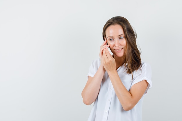 Junge Dame in der weißen Bluse, die am Telefon spricht und konzentriert schaut