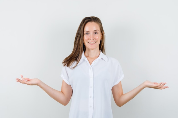 Junge Dame in der weißen Bluse, die Arme öffnet, während sie lächelt und erfreut aussieht