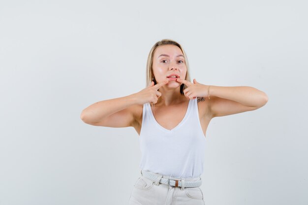 Junge Dame in der weißen Bluse, die auf ihre Zähne zeigt und konzentriert schaut