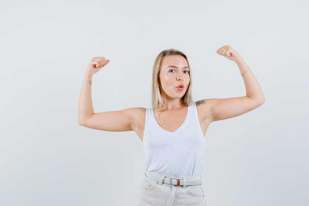 Junge Dame in der weißen Bluse, die ihre Arme hebt, ihre Muskeln zeigt und kraftvoll aussieht