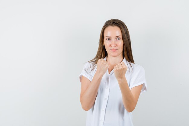 Junge Dame in der weißen Bluse, die ihre Fäuste zeigt und flexibel aussieht