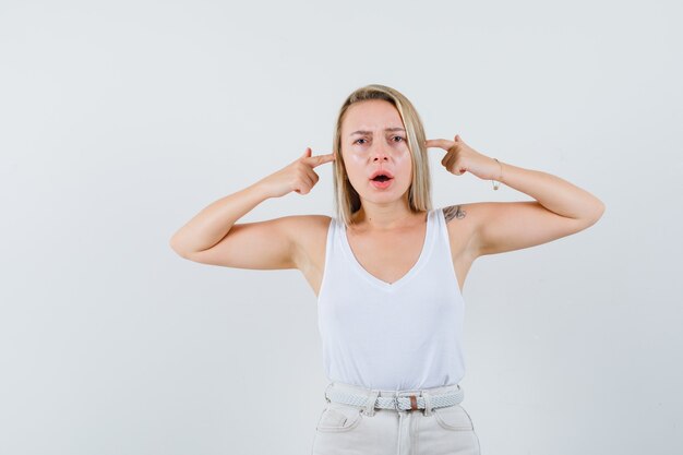 Junge Dame in der weißen Bluse, die ihre Ohren mit den Fingern verstopft und unangenehm aussieht