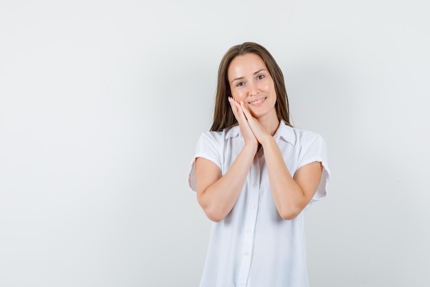 Junge Dame in der weißen Bluse, die Kissengeste zeigt und niedlich schaut