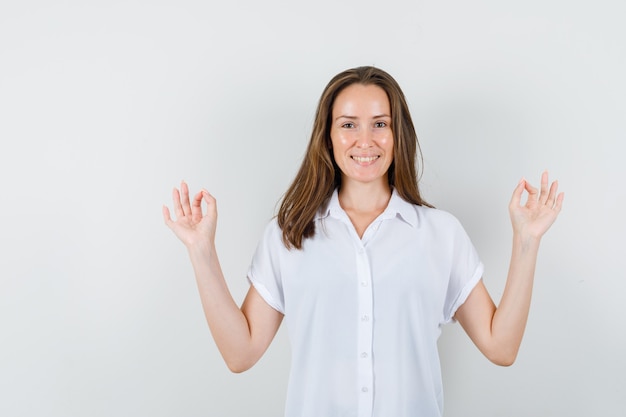 Junge Dame in der weißen Bluse, die Meditationsgeste zeigt und frisch schaut