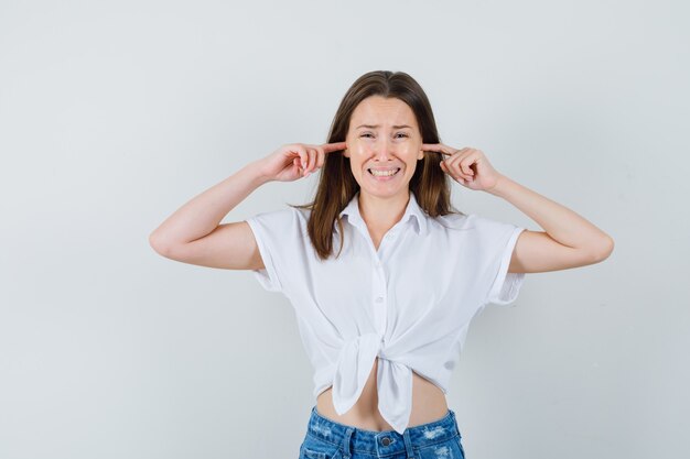 Junge Dame in der weißen Bluse, die Ohren mit den Fingern verstopft und gelangweilt, Vorderansicht schaut.