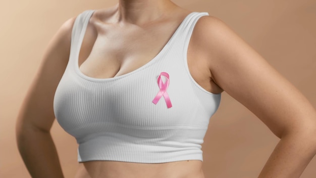 Junge Dame in einem weißen Oberteil mit einem Bandschild auf der Brust, um den rosafarbenen Oktober und Frauen zu unterstützen, die Brustkrebs bekämpfen. Anonymes Studiofoto auf beigem Hintergrund