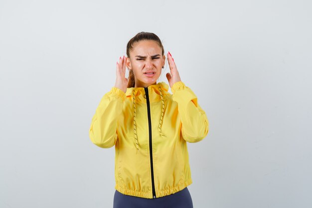 Junge Dame in gelber Jacke, die die Hände in der Nähe des Gesichts hält und aggressiv aussieht, Vorderansicht.