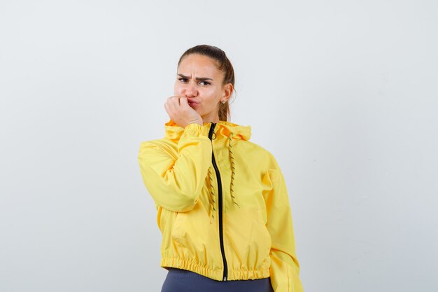 Junge Dame in gelber Jacke, die die Hand am Kinn hält und unzufrieden aussieht, Vorderansicht.