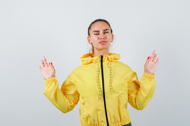 Junge Dame in gelber Jacke, die Meditationsgeste zeigt und entspannt aussieht, Vorderansicht.