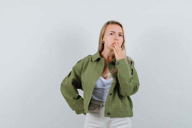 Junge Dame in Jacke, Hose, die Hand auf Mund hält und enttäuscht schaut, Vorderansicht.