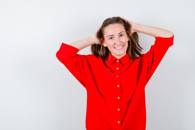 Junge Dame in roter Bluse, die die Hände auf den Kopf hält und glücklich aussieht, Vorderansicht.