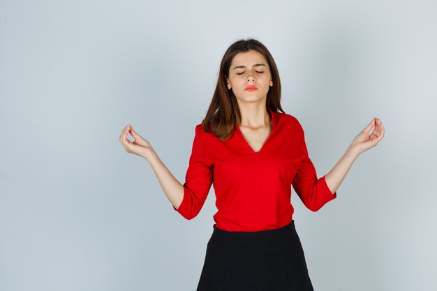 Junge Dame in roter Bluse, Rock, der Meditationsgeste zeigt und friedlich aussieht