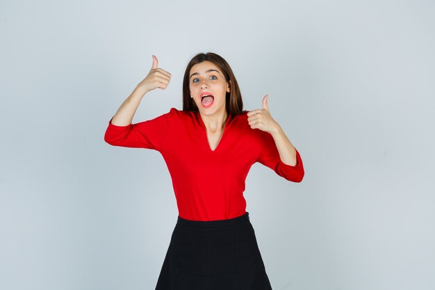 Junge Dame in roter Bluse, schwarzer Rock, der doppelte Daumen hoch zeigt und fröhlich aussieht