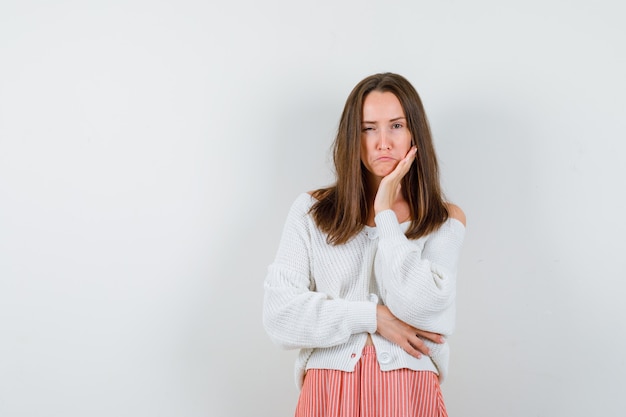 Junge Dame in Strickjacke und Rock, die Hand auf Wange hält, während lokalisiert blinkt