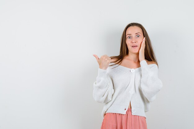 Junge Dame in Strickjacke und Rock zeigt auf die linke Seite isoliert