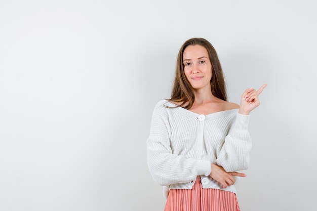 Junge Dame in Strickjacke und Rock zeigt auf die obere rechte Ecke und sieht selbstbewusst isoliert aus