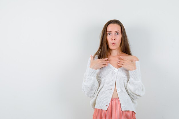 Junge Dame in Strickjacke und Rock zeigt auf sich selbst mit den Händen, die verwirrt verwirrt aussehen