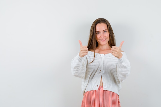 Junge dame in strickjacke und rock zeigt daumen hoch und schaut glücklich isoliert