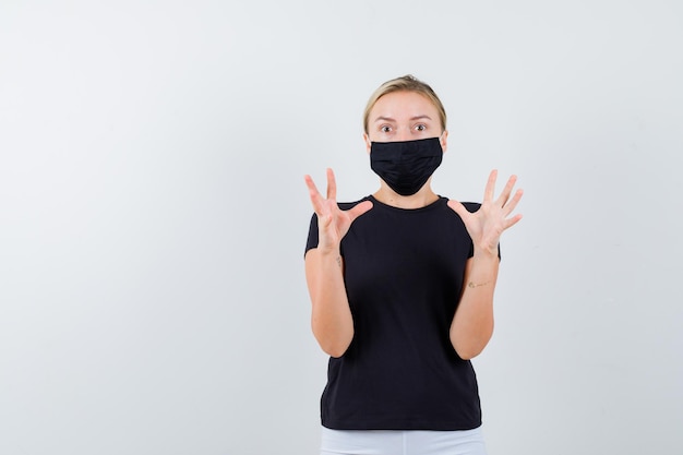 Junge Dame in T-Shirt, Hose, medizinischer Maske, die die Hände auf aggressive Weise hält