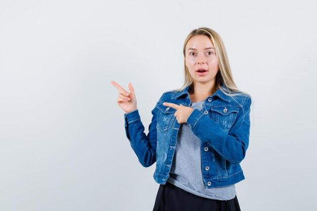 Junge Dame in T-Shirt, Jeansjacke, Rock zeigt zur Seite und sieht erstaunt aus