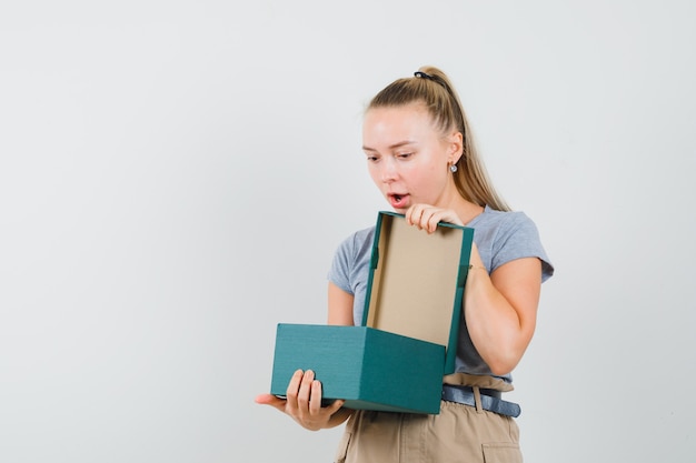 Junge Dame in T-Shirt und Hose, die in Geschenkbox schaut und erstaunt schaut