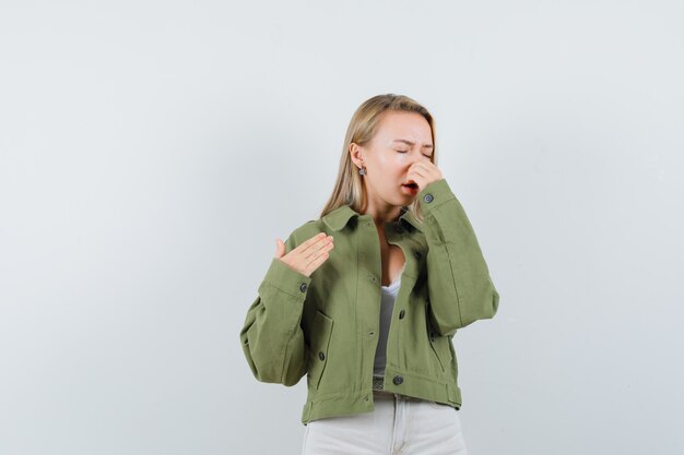 Junge Dame kneift die Nase wegen des schlechten Geruchs in Jacke, Hose und sieht angewidert aus, Vorderansicht.