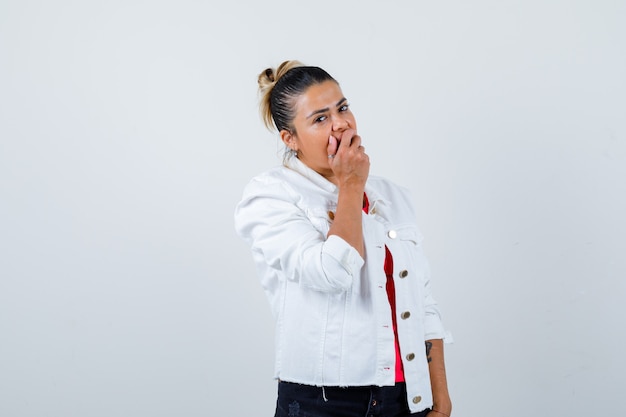 Junge Dame mit der Hand auf dem Mund im T-Shirt, in der weißen Jacke und in der Vorderansicht verwirrt.