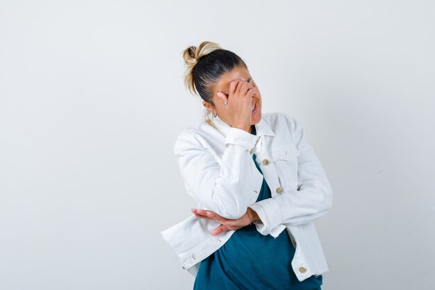 Junge Dame mit der Hand im Gesicht im Hemd, in der weißen Jacke und im glücklichen Schauen. Vorderansicht.