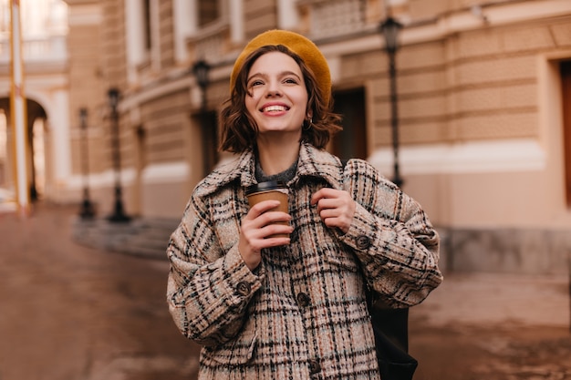 Kostenloses Foto junge dame mit nacktem make-up lächelt aufrichtig gegen stadtmauer