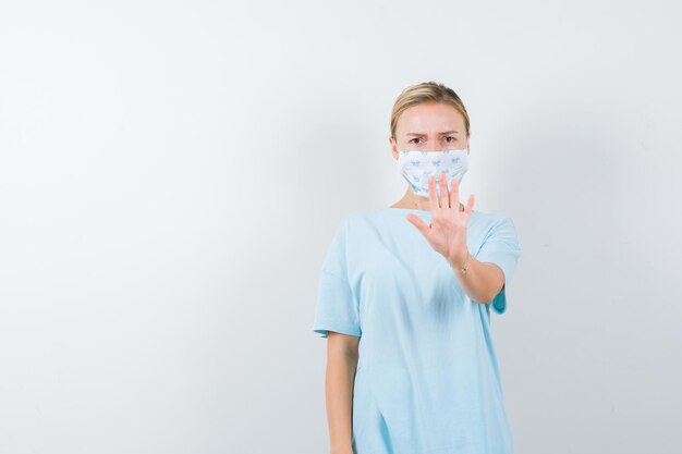 Junge Dame mit Stopp-Geste in T-Shirt, Maske und ernstem Blick