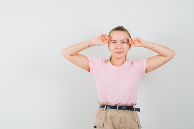 Junge Dame posiert beim Berühren ihrer Gesichtshaut in T-Shirts und Hosen und sieht zart aus