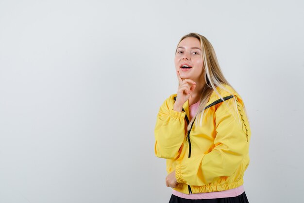 Junge Dame posiert beim Stehen im T-Shirt, in der Jacke und im verführerischen Blick