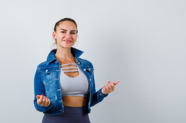 Junge Dame posiert in Top, Jeansjacke und sieht fröhlich aus, Vorderansicht.