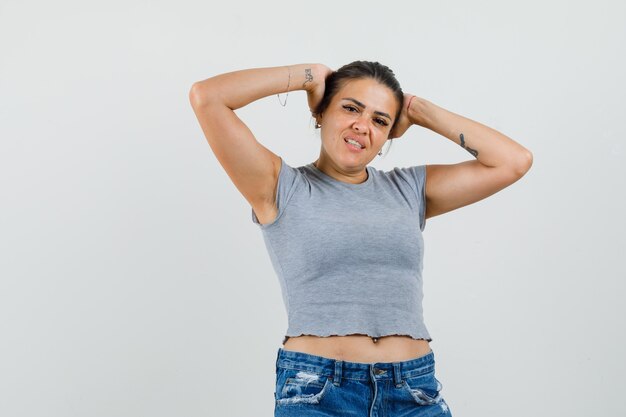 Junge Dame posiert, während sie ihren Kopf in T-Shirt, Shorts umschließt und attraktiv aussieht