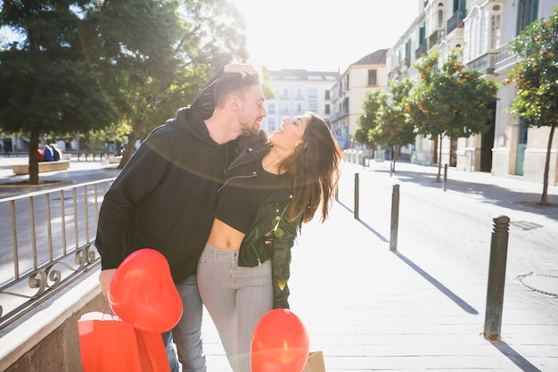 Junge Dame und lächelnder Kerl mit den Paketen und Ballonen, die Spaß auf Straße haben