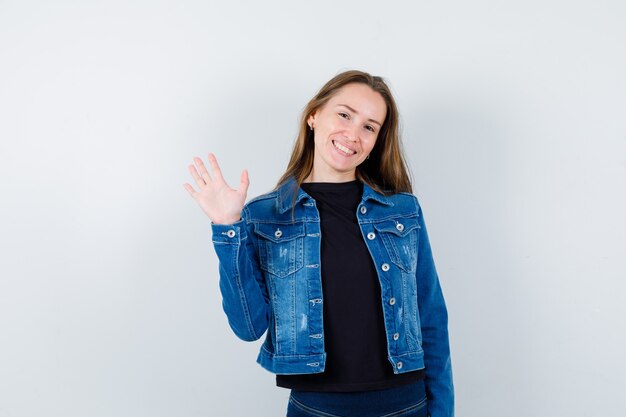 Junge Dame winkt mit der Hand zum Gruß in der Bluse und sieht glücklich aus. Vorderansicht.