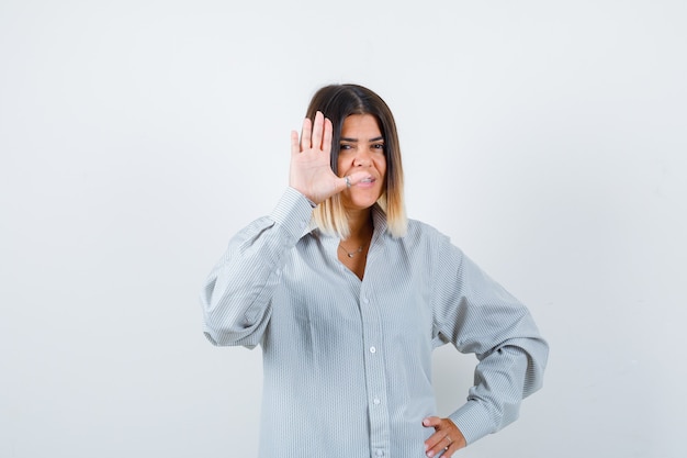 Junge Dame winkt mit der Hand zum Gruß in übergroßem Hemd und sieht zufriedene Vorderansicht aus.