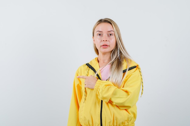 Junge Dame zeigt auf die linke Seite in T-Shirt, Jacke und sieht selbstbewusst aus