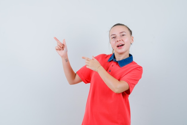 Junge Dame zeigt auf die obere linke Ecke im T-Shirt und sieht munter aus