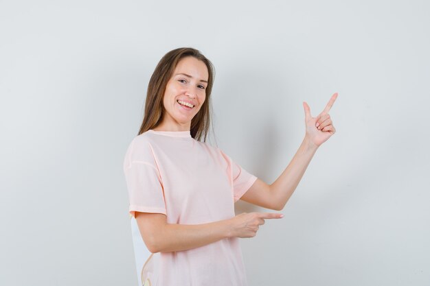 Junge Dame zeigt auf die obere rechte Ecke im rosa T-Shirt und schaut fröhlich, Vorderansicht.