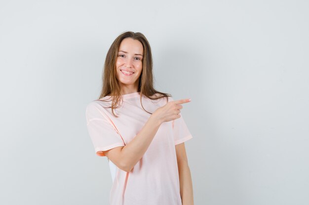 Junge Dame zeigt auf die rechte Seite im rosa T-Shirt und sieht selbstbewusst aus. Vorderansicht.