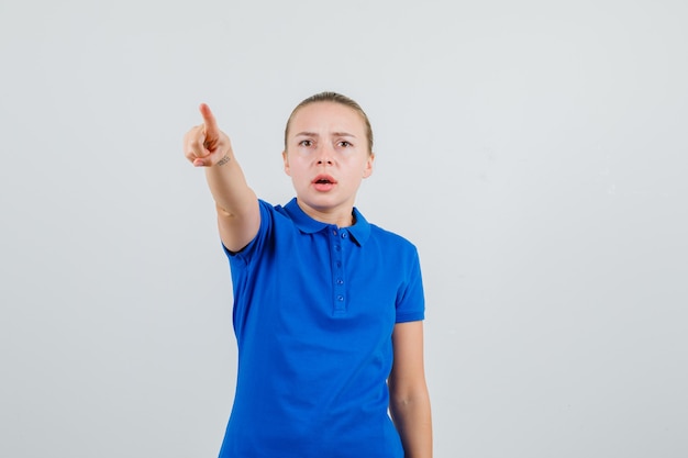 Junge Dame zeigt auf etwas weg im blauen T-Shirt und sieht nervös aus