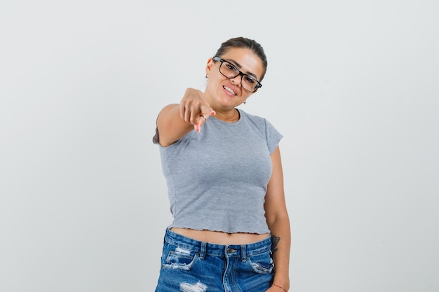 Junge Dame zeigt auf Kamera in T-Shirt, Shorts und schaut selbstbewusst