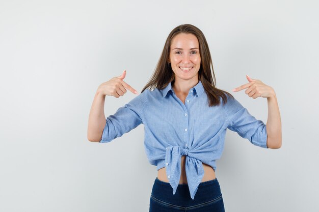 Junge Dame zeigt auf sich in blauem Hemd, Hose und sieht selbstbewusst aus