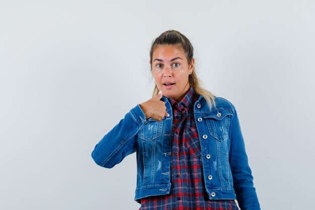 Junge Dame zeigt auf sich selbst in Hemd, Jacke und sieht verwirrt aus. Vorderansicht.