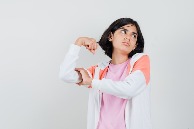 Junge Dame zeigt ihre Armmuskeln in Jacke, rosa Hemd und sieht nachdenklich aus.