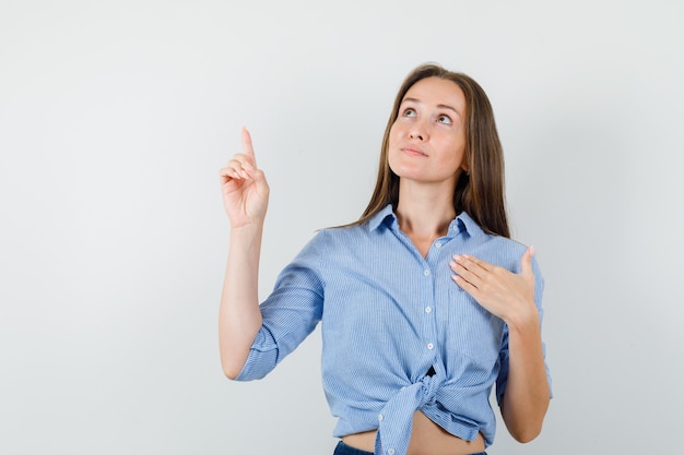 Junge Dame zeigt in blauem Hemd, Hose und hoffnungsvoll